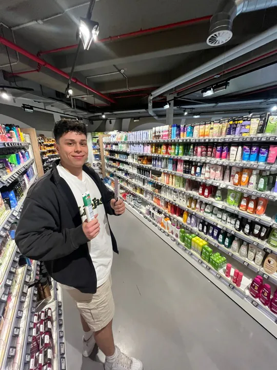 Kollege hält im Gang eines Drogeriemarkts zwei Produkte in die Kamera