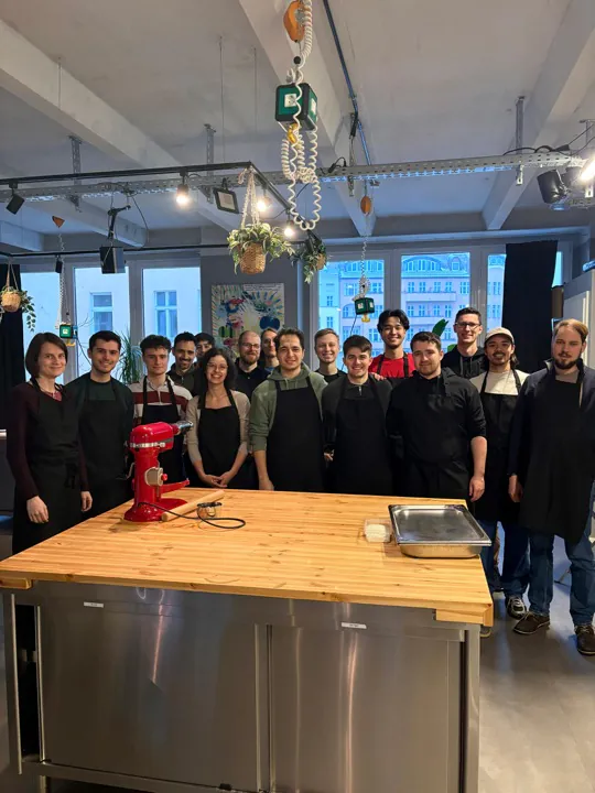 Das Team in Schürzen um die Kücheninsel eines Kochstudios