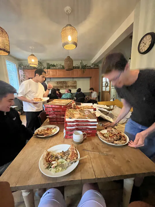 Langer Tisch voller Pizzakartons, Kollegen holen sich Stücke