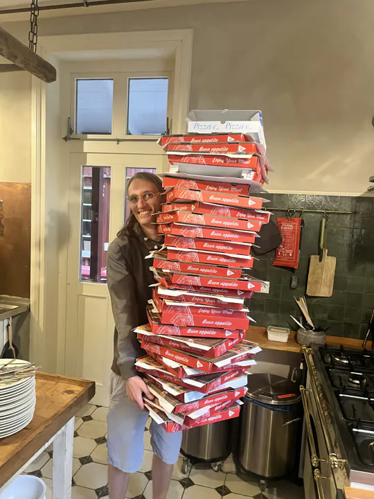 Kollege trägt einen hohen Stapel Pizzakartons durch eine Küche