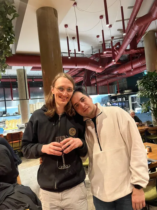 Zwei Kollegen Arm in Arm in einem Restaurant, einer mit einem Glas Wein